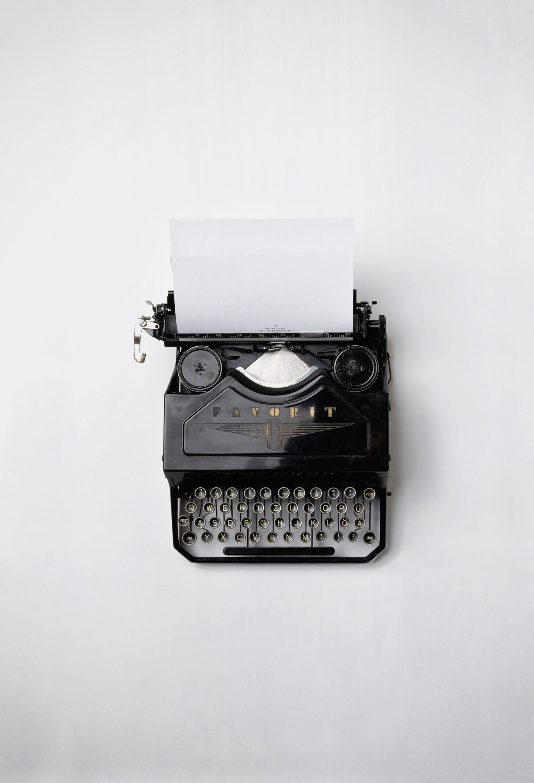 black typewriter with paper sticking out of it and a white background behind it.