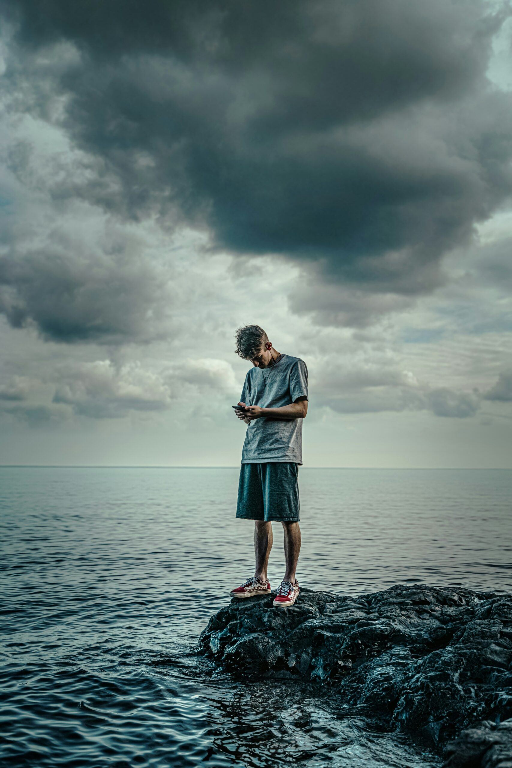 A man standing on a rock near the ocean looking at his phone