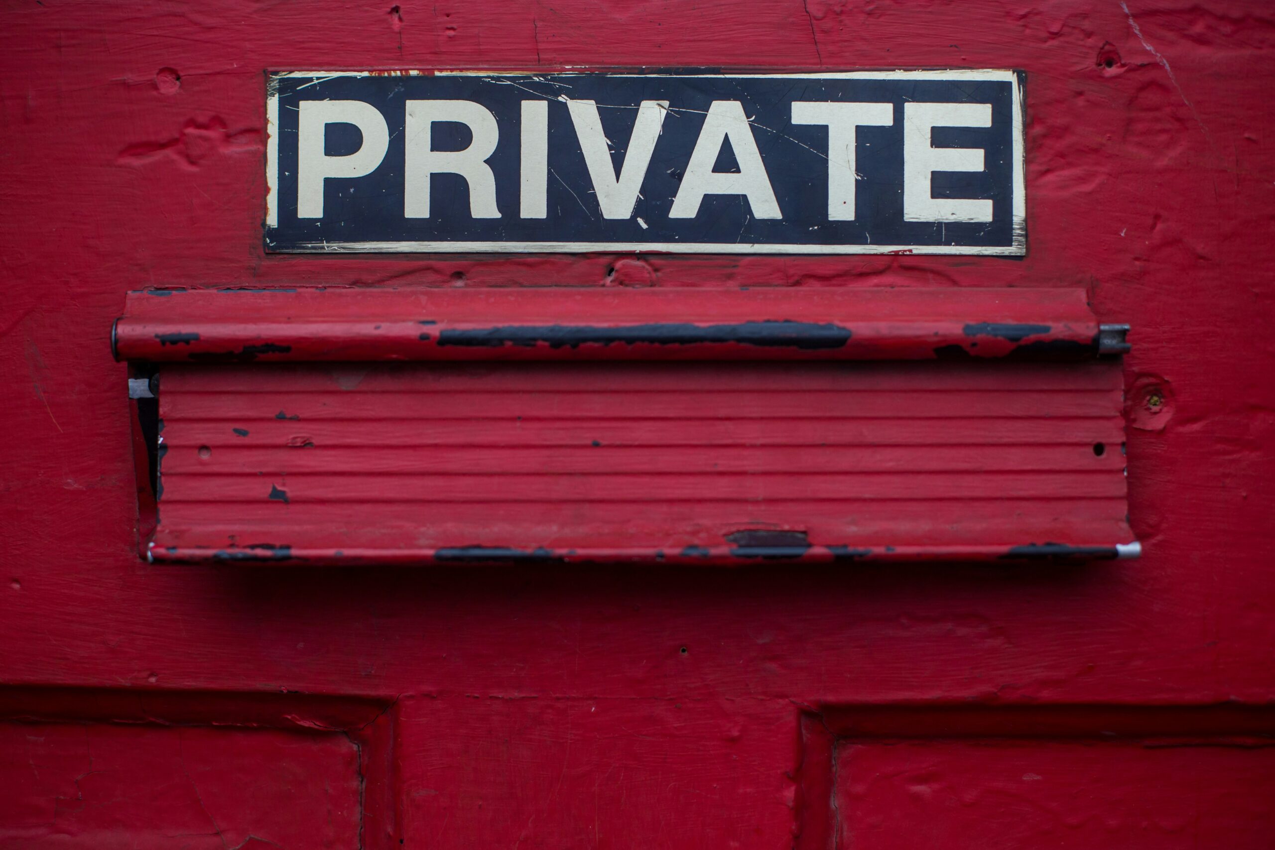 Close-up of a red door with a "PRIVATE" sign in bold white letters on a black background, highlighting privacy and restricted access.