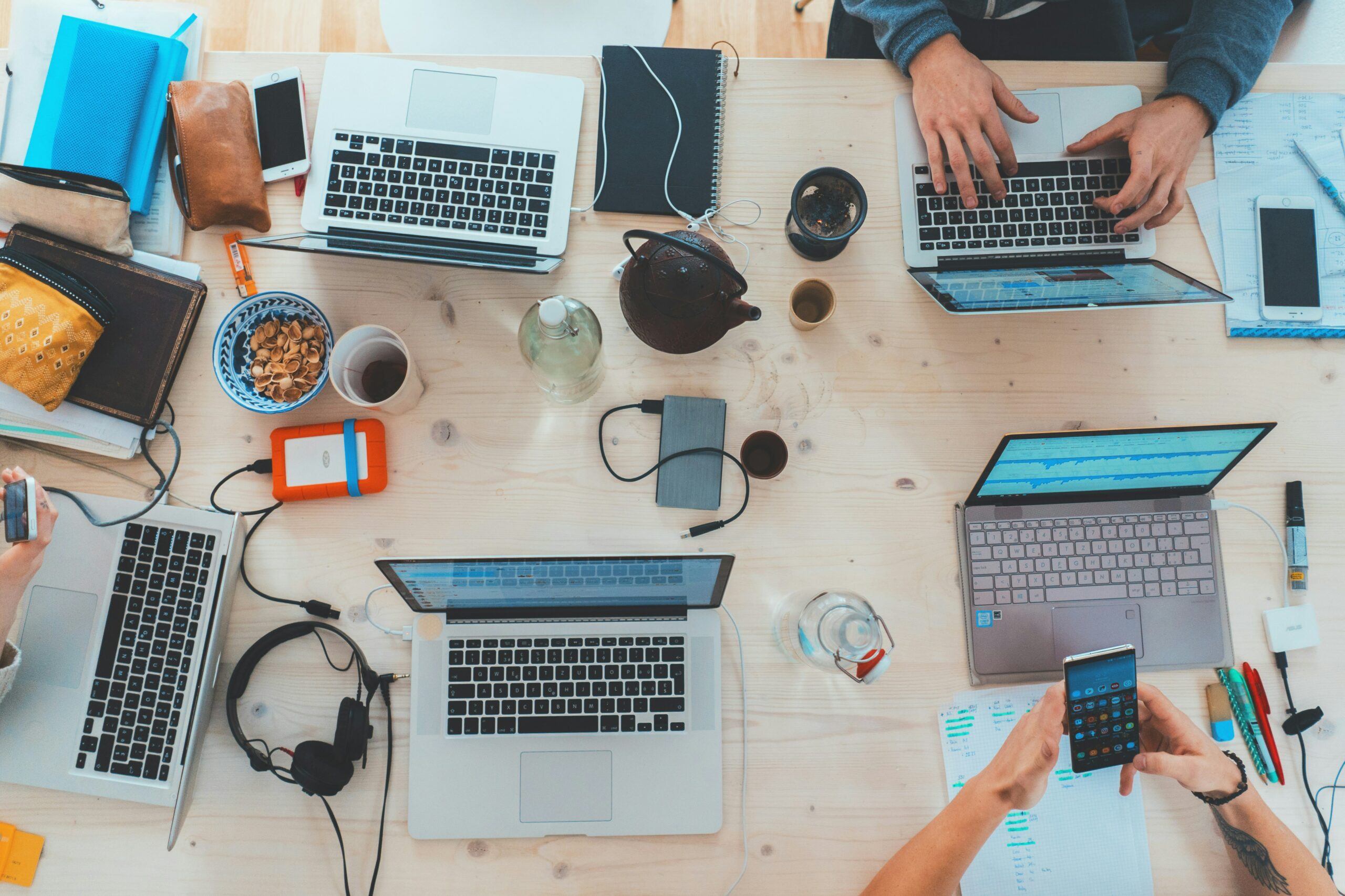 People sitting at a desk using phones, laptops, and other technology.