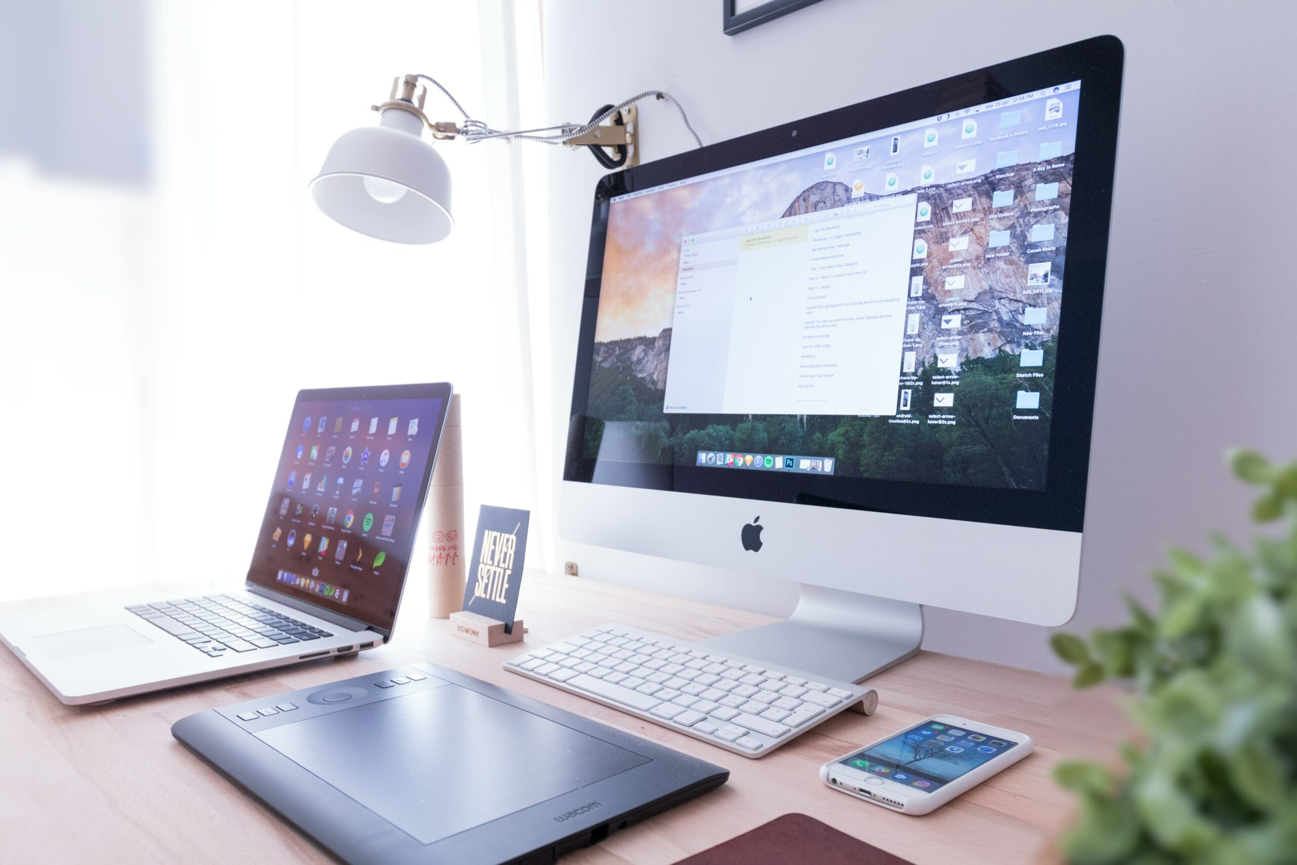 Mac desktop, Mac laptop, Iphone and Ipad all being used at once, sitting on a desk.