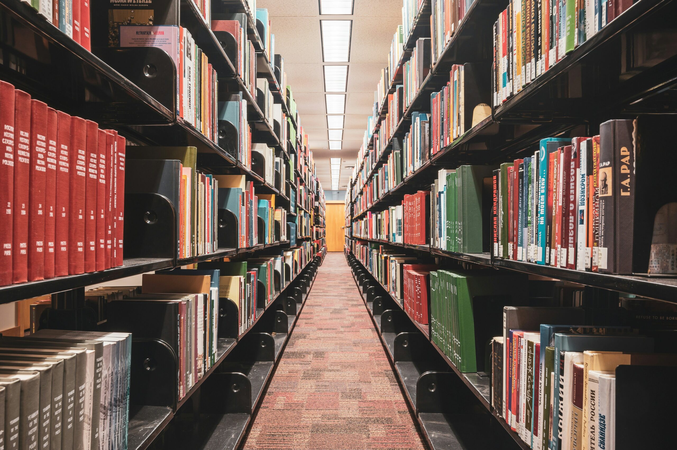 A row in a library with shelves filled with books on either side and a yellow door at the end of the aisle.