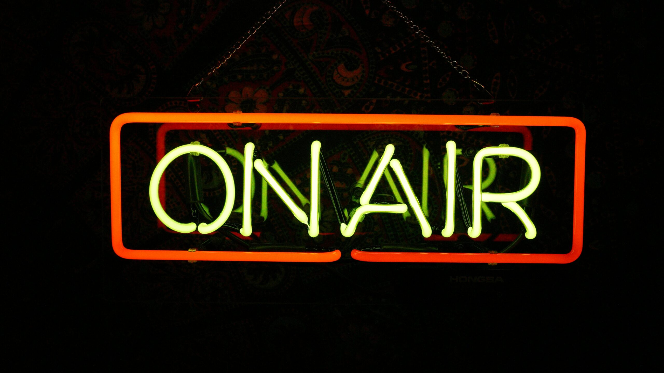 Neon sign with the word "ON AIR" illuminated in green and orange against a dark background.