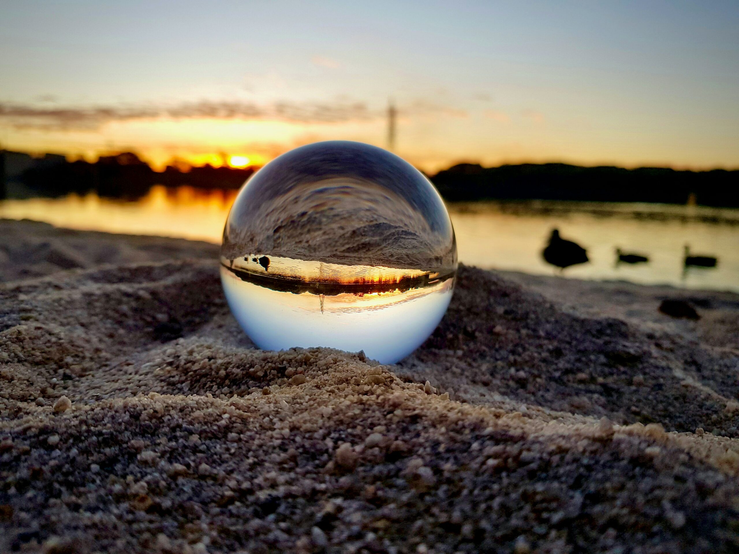 An image of a ball of water on sand reflecting the view behind.