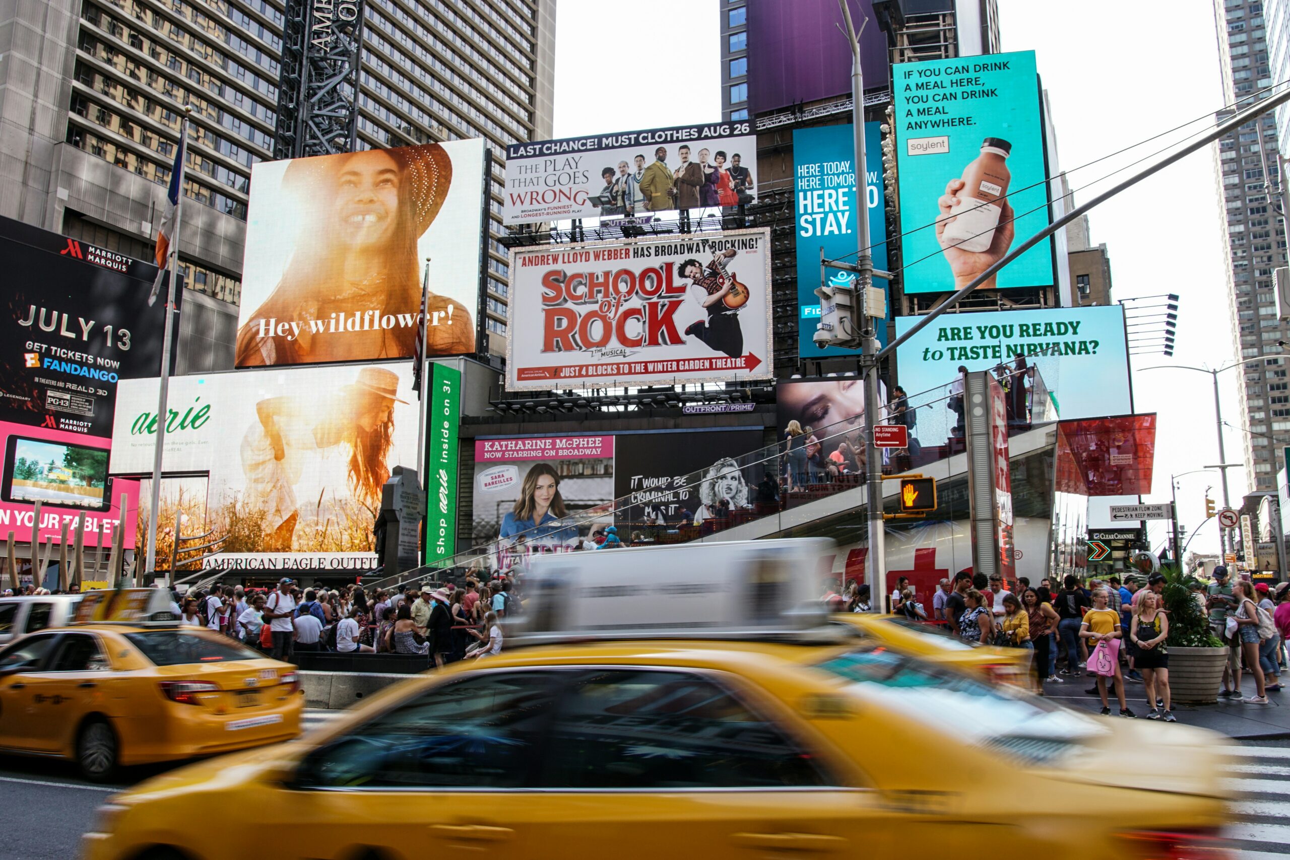 Times Square billboards lit up behind busy traffic and people walking.