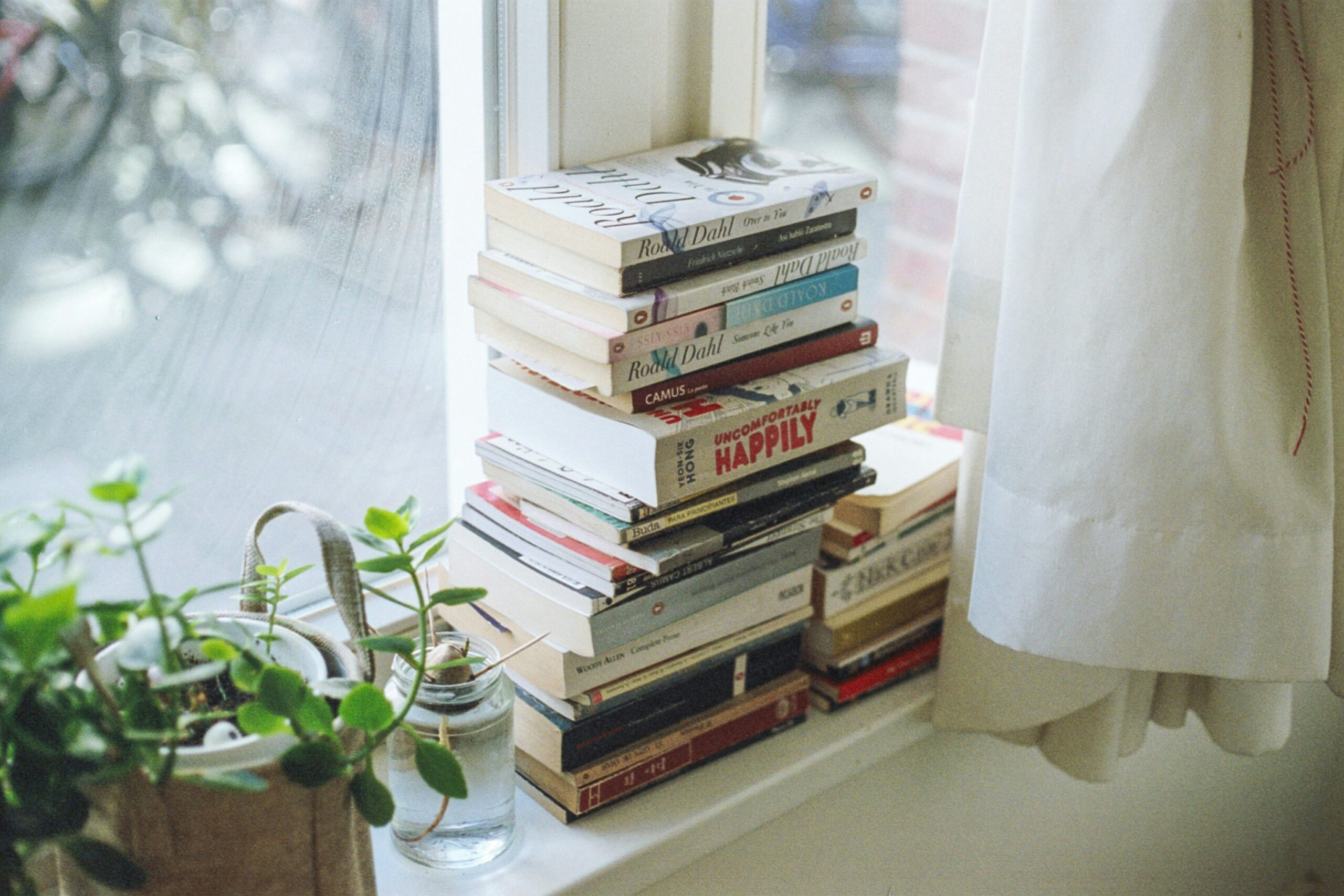 Pile of books at a window sill being lit by light sunshine; meant to represent visual storytelling.