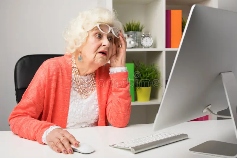 Photo of an elderly woman looking very stressed out at her computer screen.