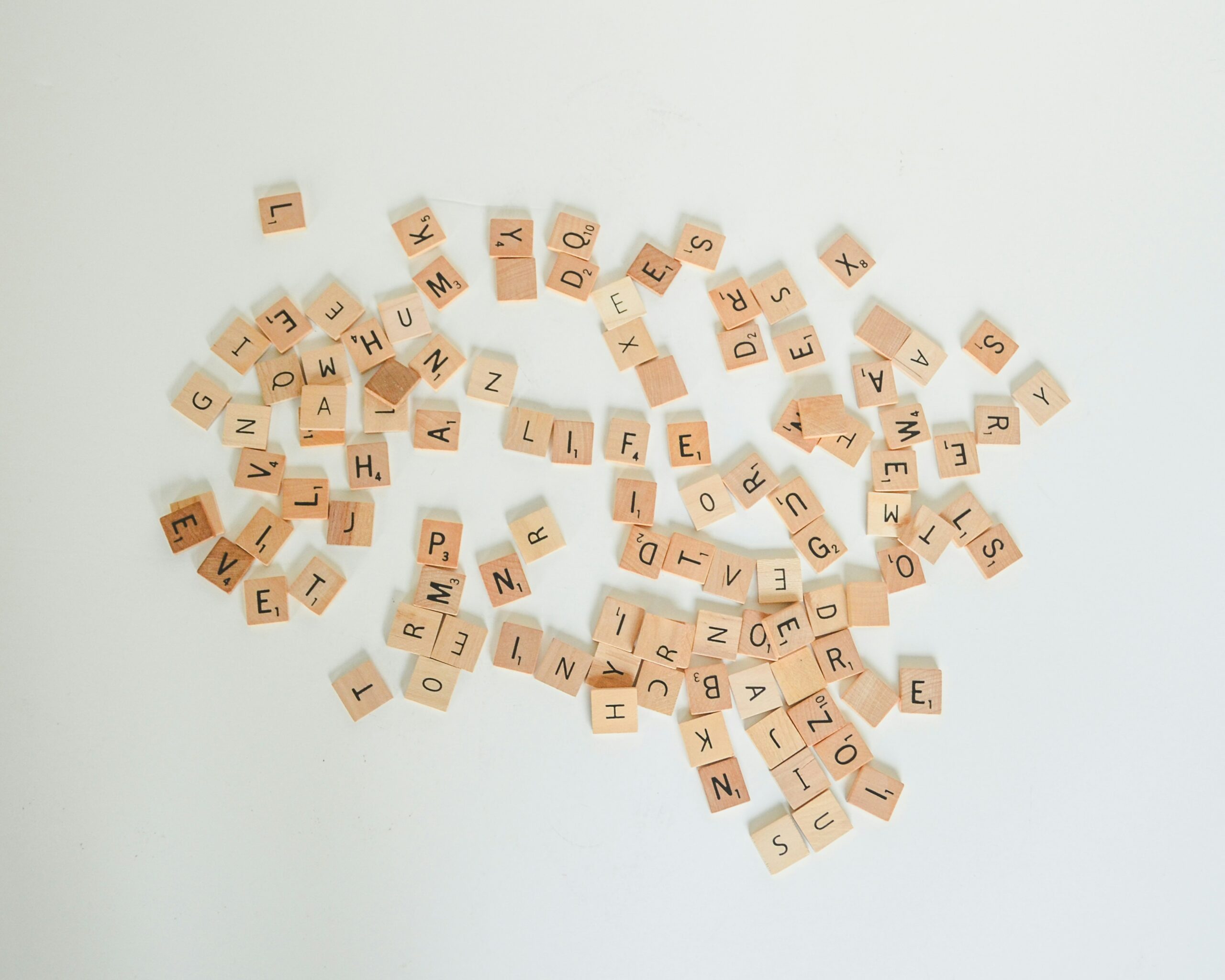 In the photo there are different scrabble pieces (small wood square pieces with different letters on it) placed all over.