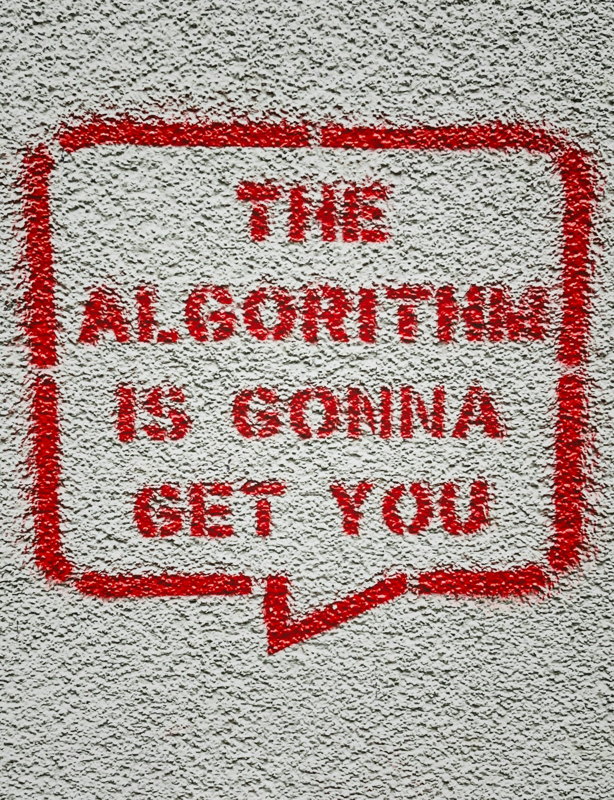 A white wall with the sentence "The algorithm is gonna get you" that shows the effect of digital rhetoric.